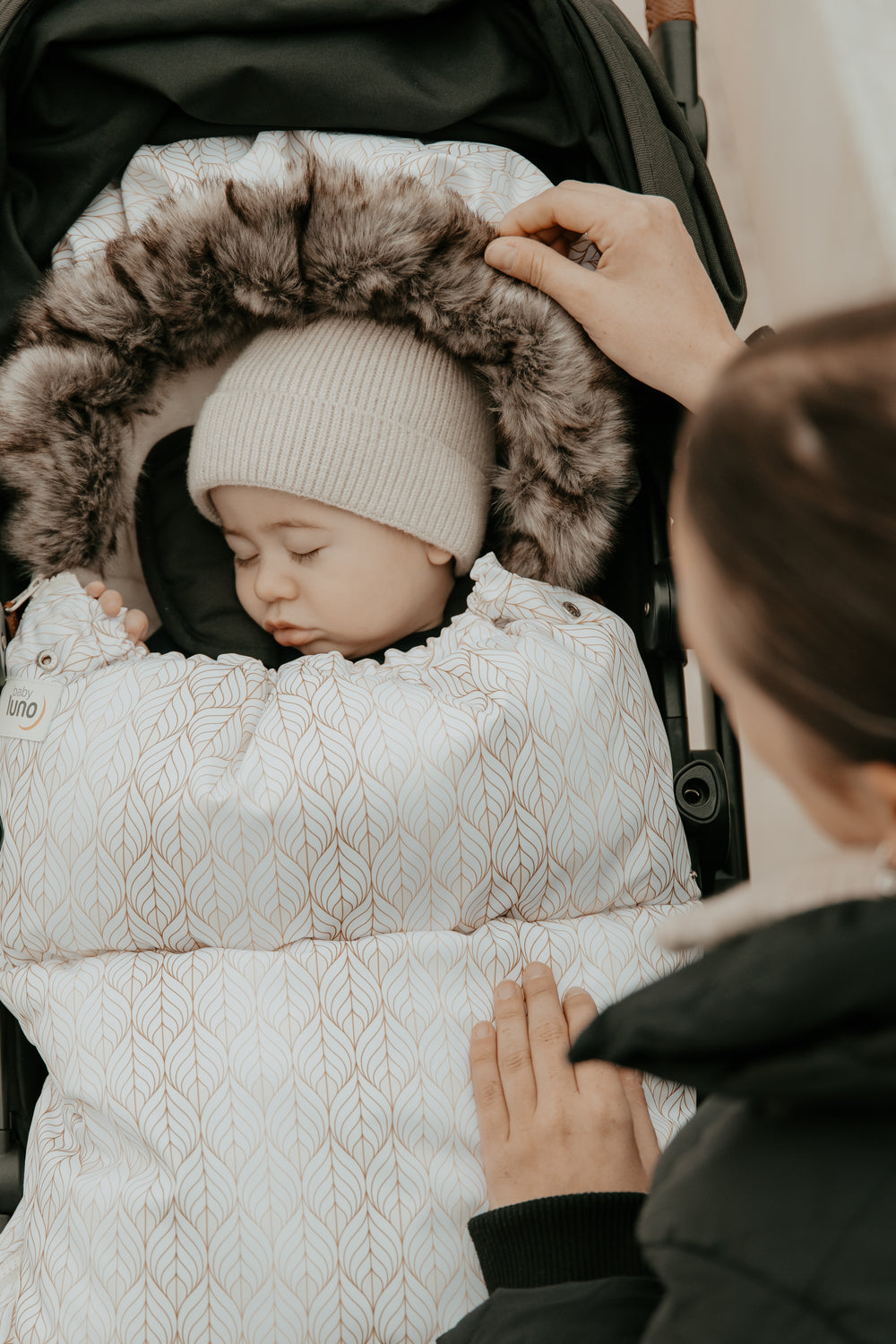 Baby sleeping in a stroller with a patterned swaddle blanket on a neutral background