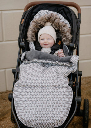 Baby in a stroller in baby luno footmuff wearing a cream beanie