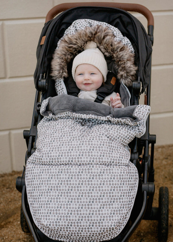 Baby in a stroller in baby luno footmuff wearing a cream beanie