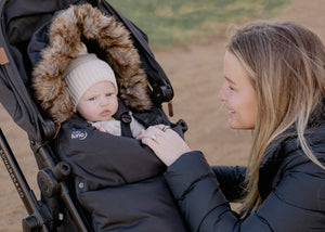 Mum and Baby in a black baby luno footmuff and white knitted hat with pom-pom.