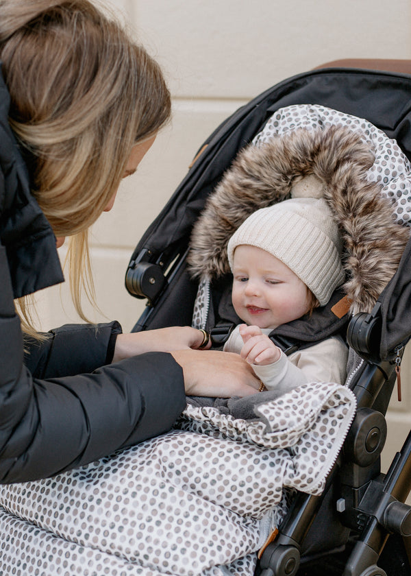 Baby in Raindrops baby luno footmuff stroller liner wearing ivory beanie
