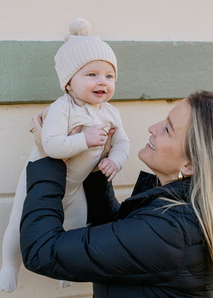 Mother holding a baby wearing a white outfit and knit hat.