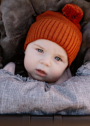 Baby wearing an orange brown knit hat with a pom-pom.