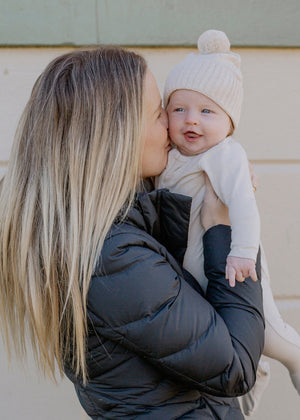 Mum kissing her baby wearing a white outfit and beige hat