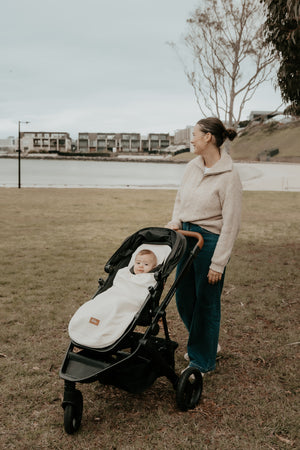 Mother pushing a stroller with a baby in it wrapped up in the baby luno summer footmuff blanket