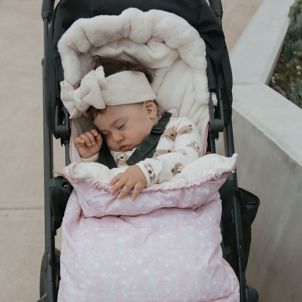 Baby in a stroller with a pink and white footmuff pram liner baby luno