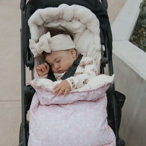 Baby in a stroller with a pink and white footmuff pram liner baby luno