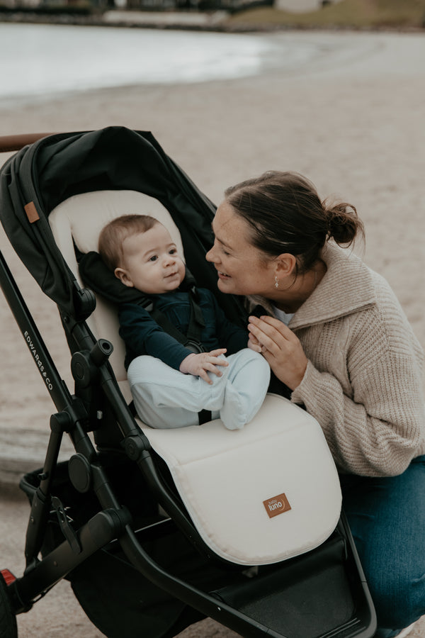 Mother sitting on a beach with a baby in a stroller on the baby luno pram liner