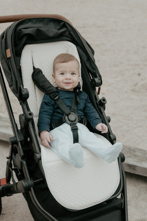 Baby sitting in a stroller with a cream cushion pram liner waffle