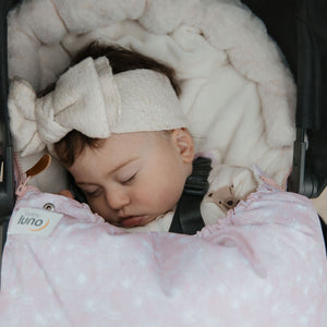 Baby sleeping in a stroller in a cosy pink footmuff and white bow headband.