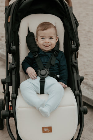 Baby sitting on baby luno Lite Summer Footmuff smooth cream pram liner side.