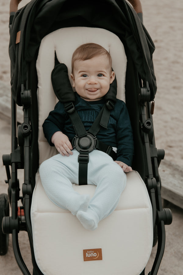 Baby sitting on baby luno Lite Summer Footmuff smooth cream pram liner side.
