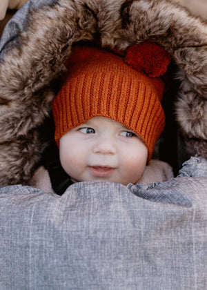 Baby wearing rust knit beanie in Chic Grey baby luno footmuff