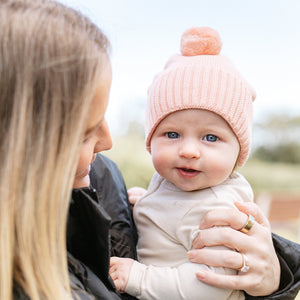 Woman holding a baby wearing a pink knit hat outdoors