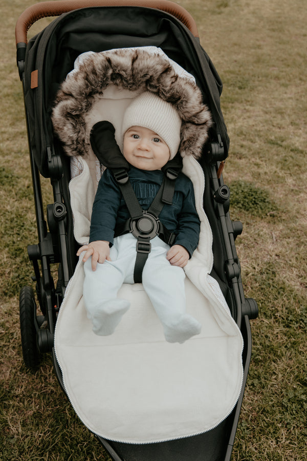 Baby in a stroller with a fur-lined hood baby luno footmuff on a grassy background